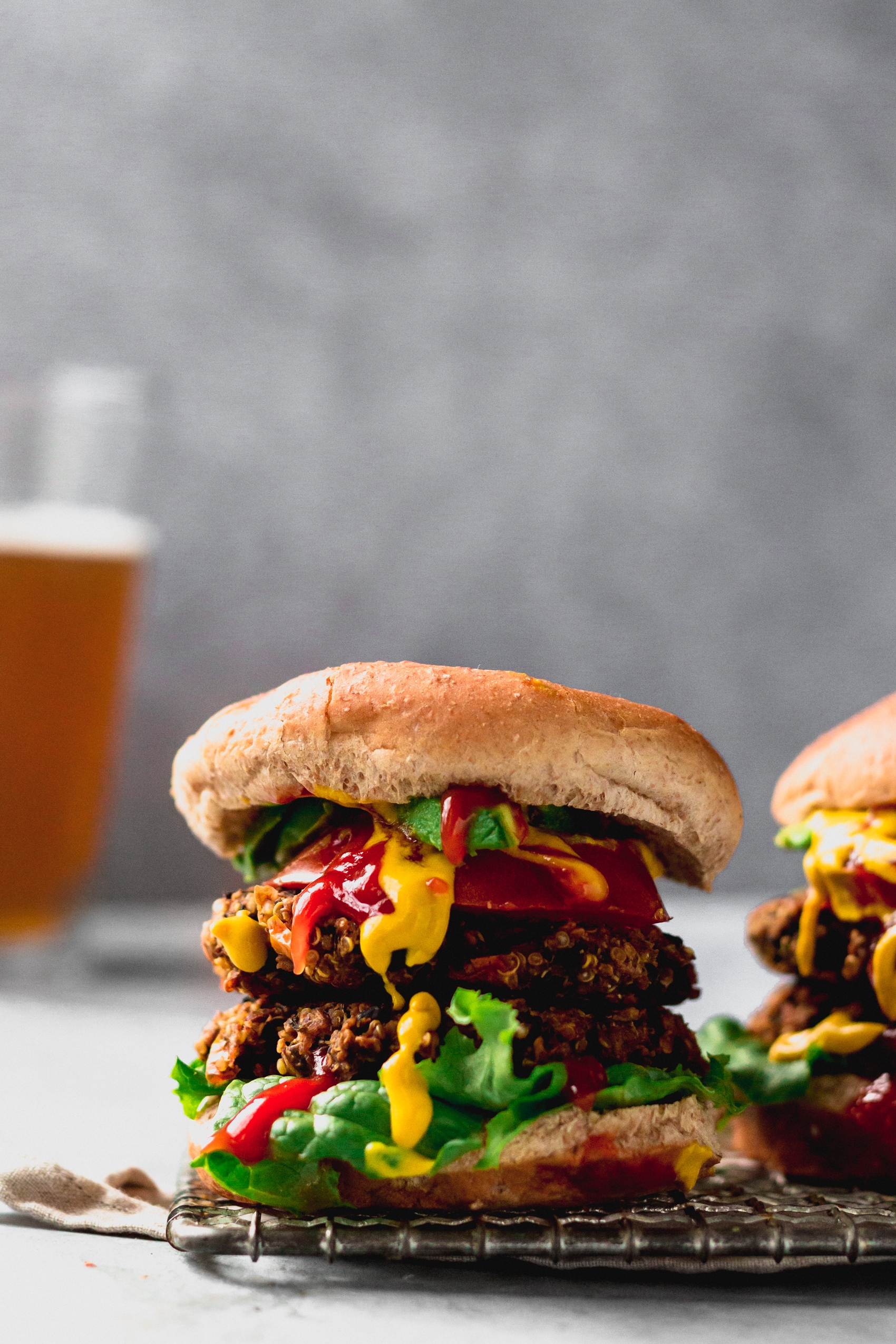 two veggie burgers with two patties each served on a cooling rack with a glass of beer in the background