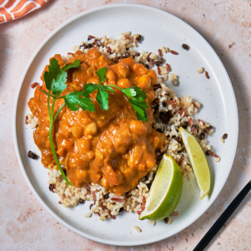 a plate of grains topped with pumpkin curry served with two lime wedges