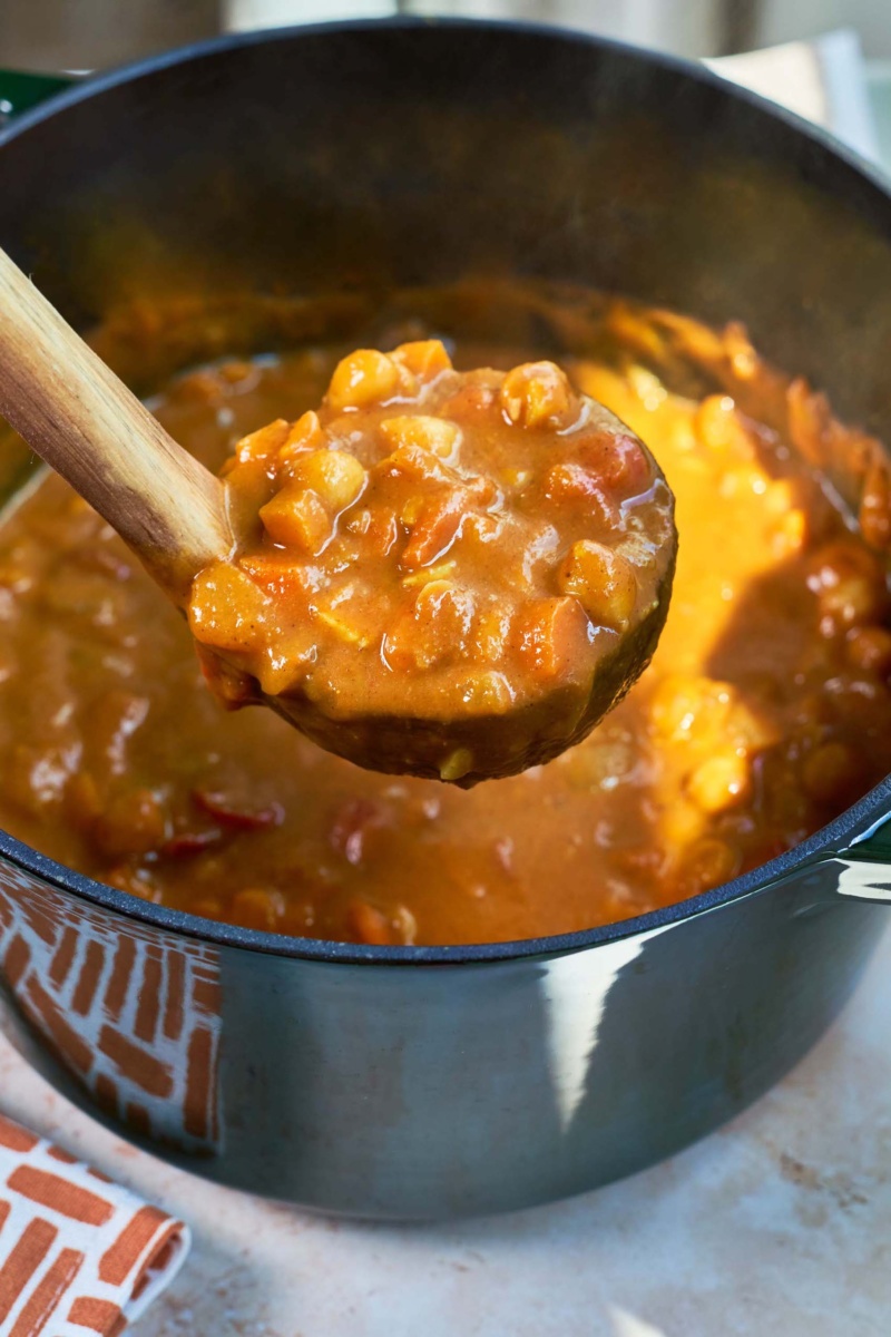 a ladle of pumpkin curry being scooped out of a stock pot