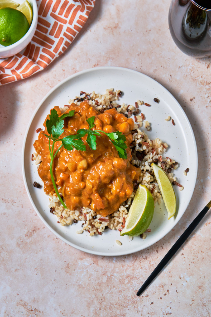 a plate of grains topped with chickpea curry served with lime wedges