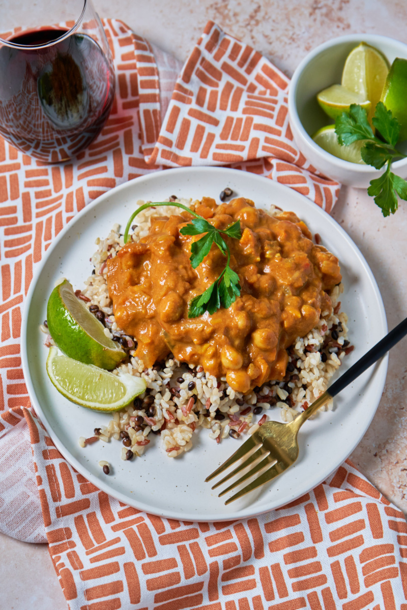 a plate of pumpkin curry served over grains alongside lime wedges and a glass of red wine