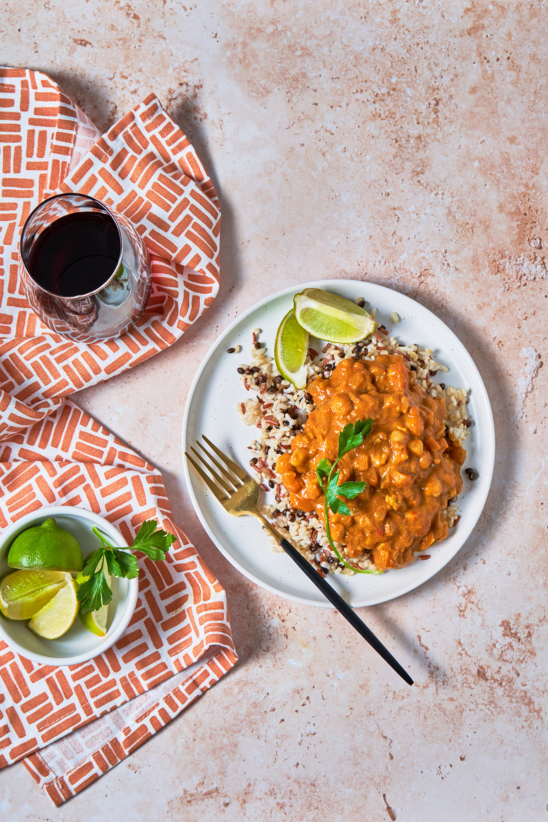 a plate of grains topped with coconut pumpkin curry served with lime wedges