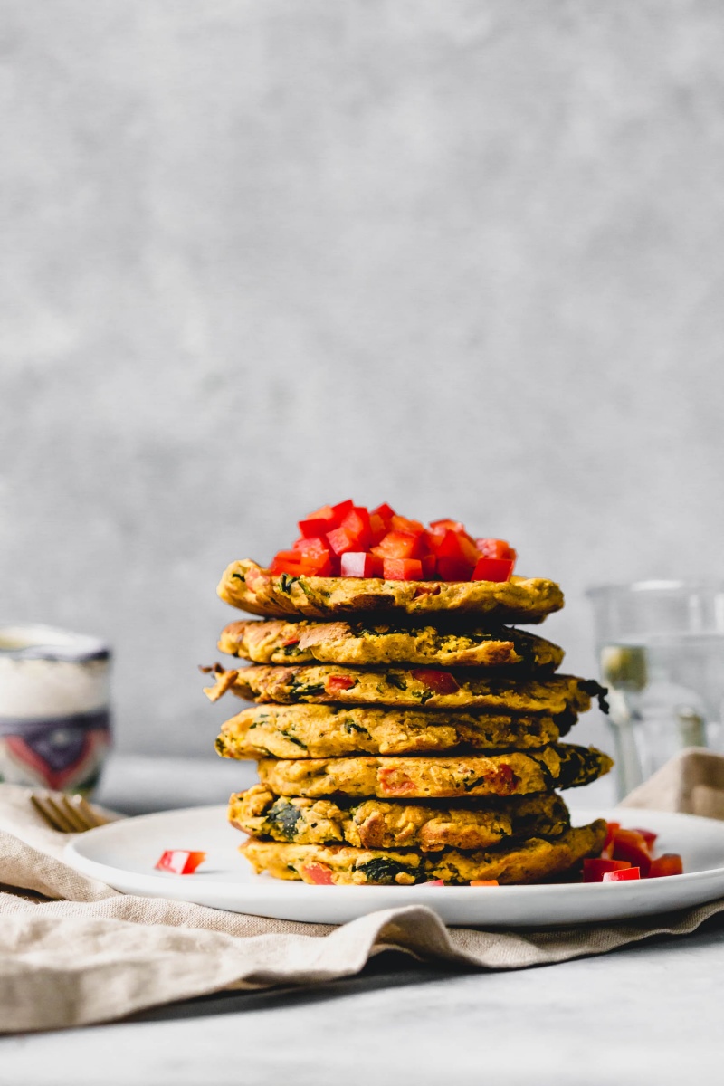 a stack of 7 chickpea pancakes topped with chopped bell pepper
