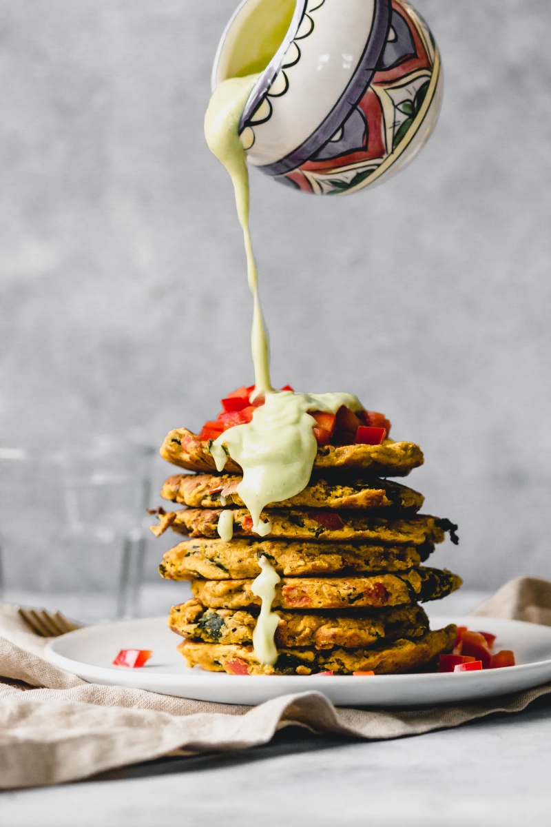 an avocado sauce is poured overtop a stack of chickpea pancakes