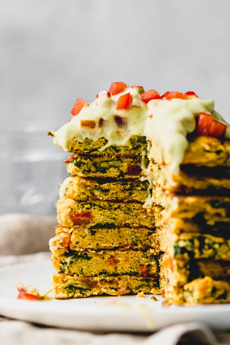 a stack of chickpea pancakes topped with a homemade avocado sauce and diced bell pepper