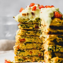 a stack of chickpea pancakes topped with avocado sauce