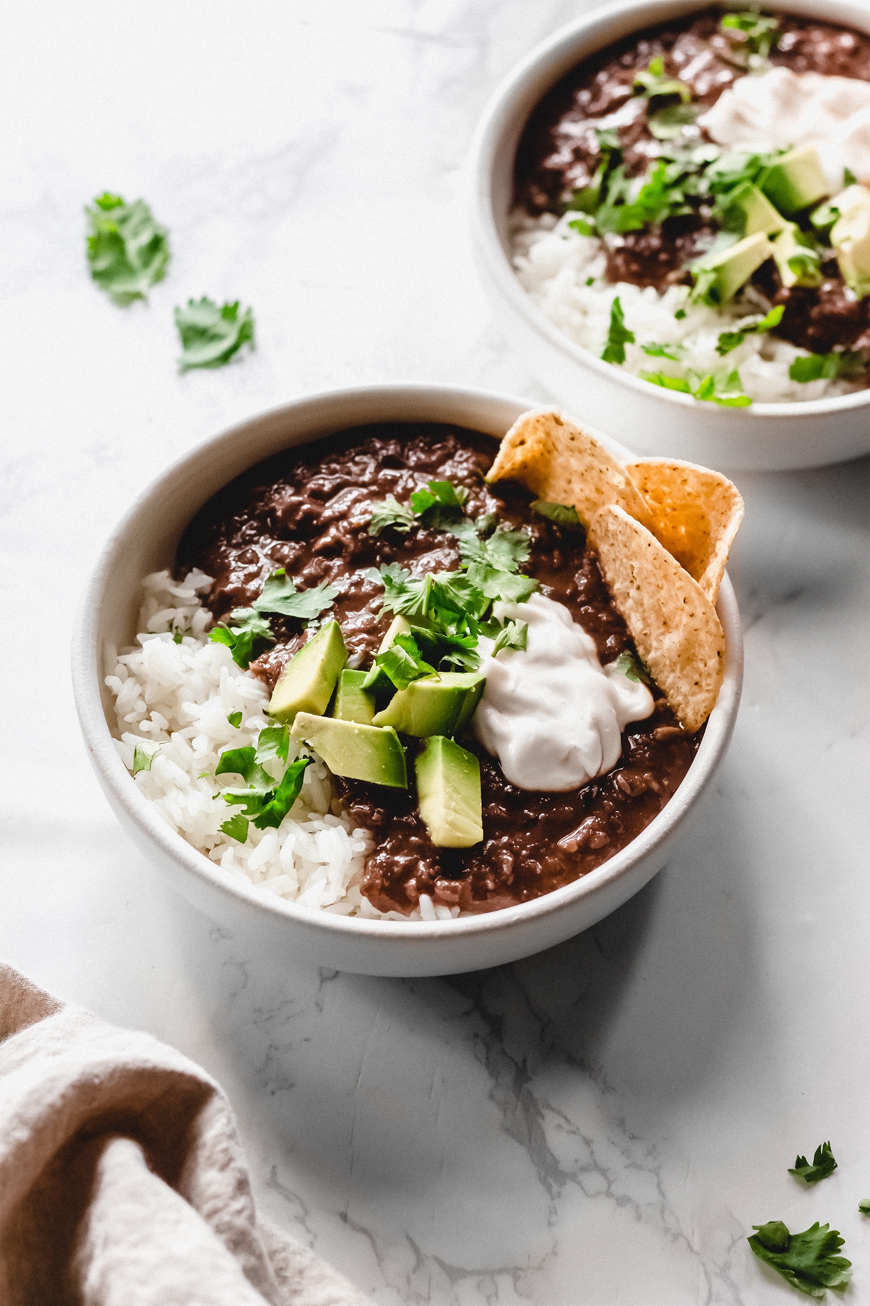 two bowls of black bean soup served with avocado and tortilla chips