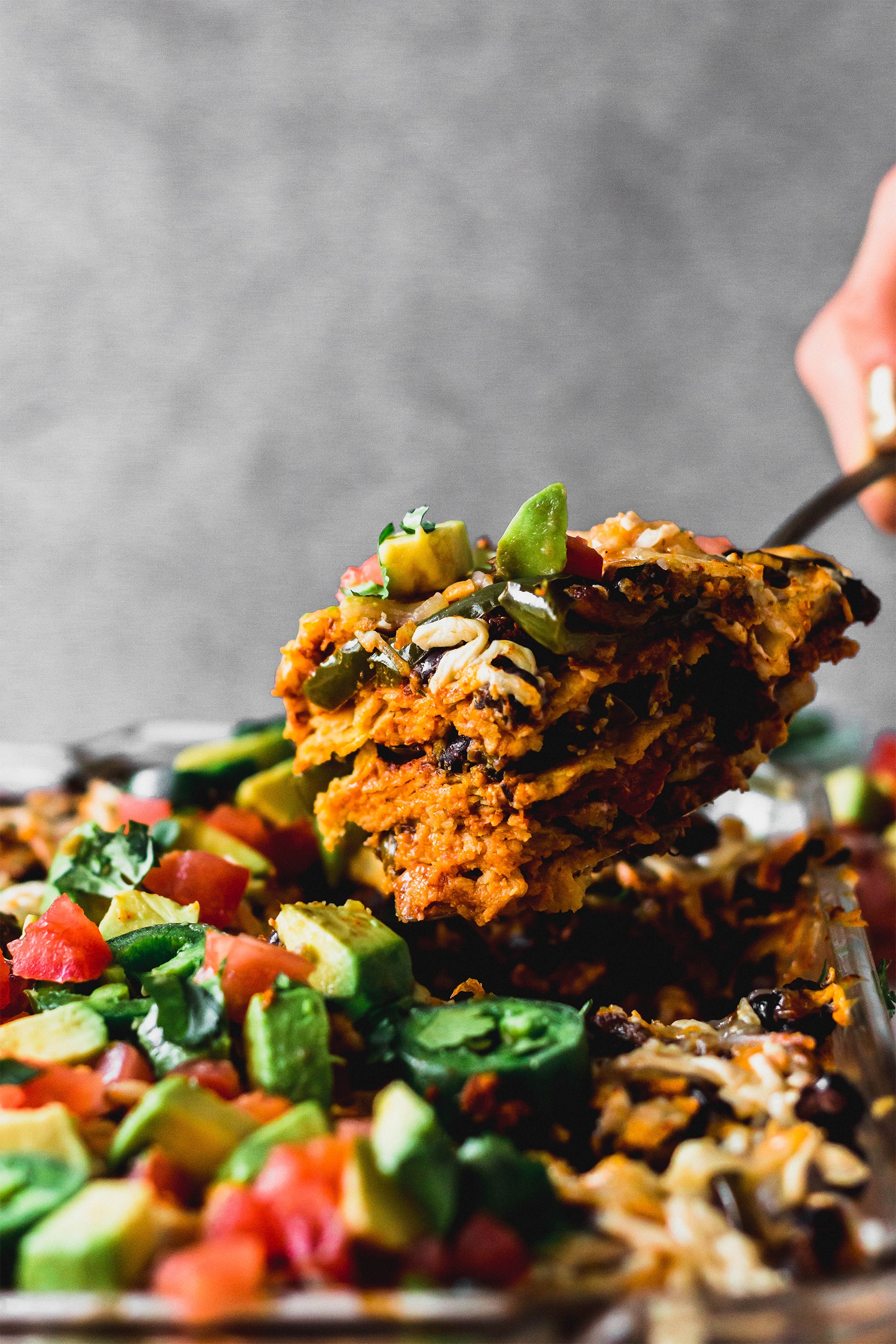 a slice of vegan enchilada casserole being scooped out of a casserole dish