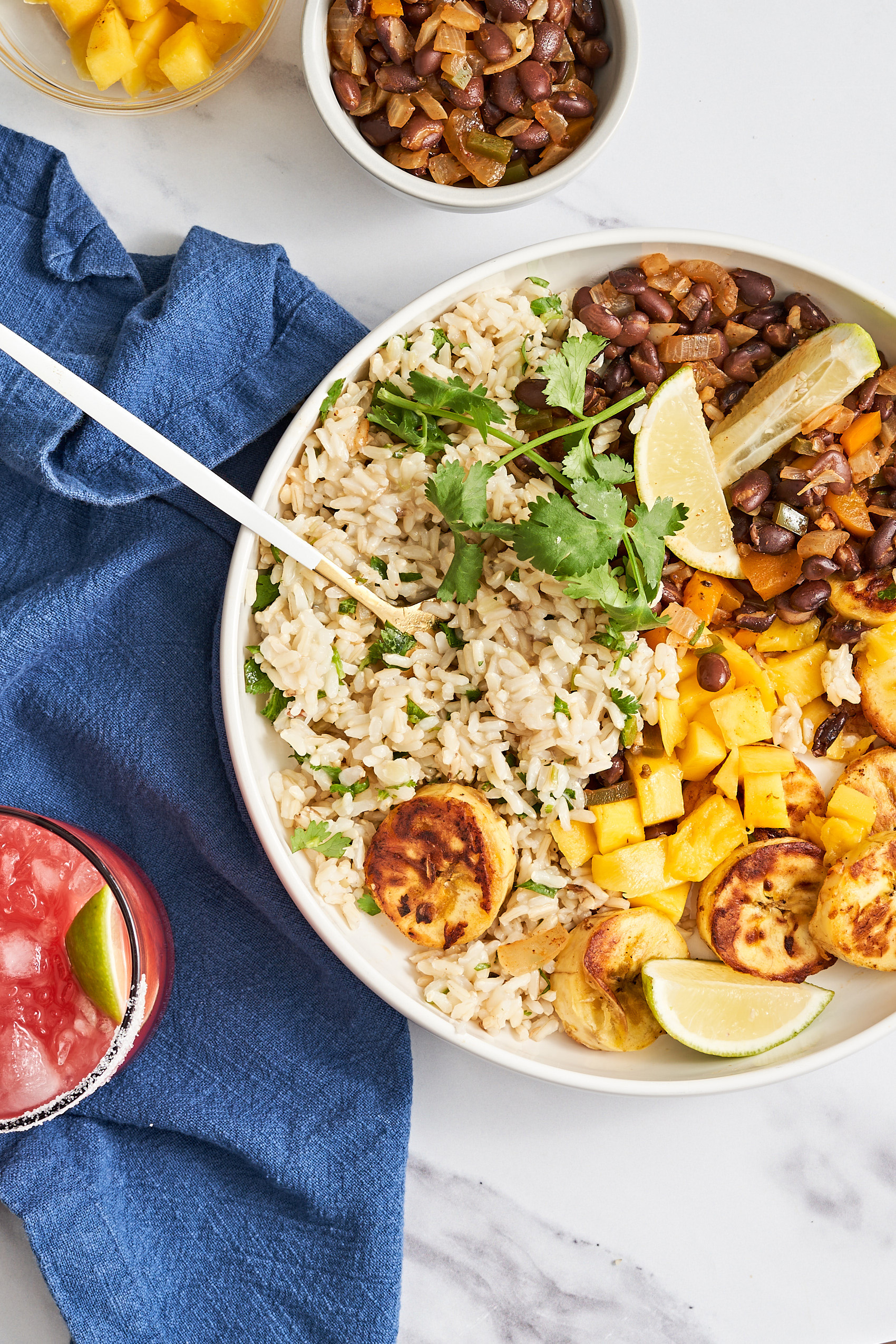a bowl of rice topped with fried plantains, black beans, mango and cilantro