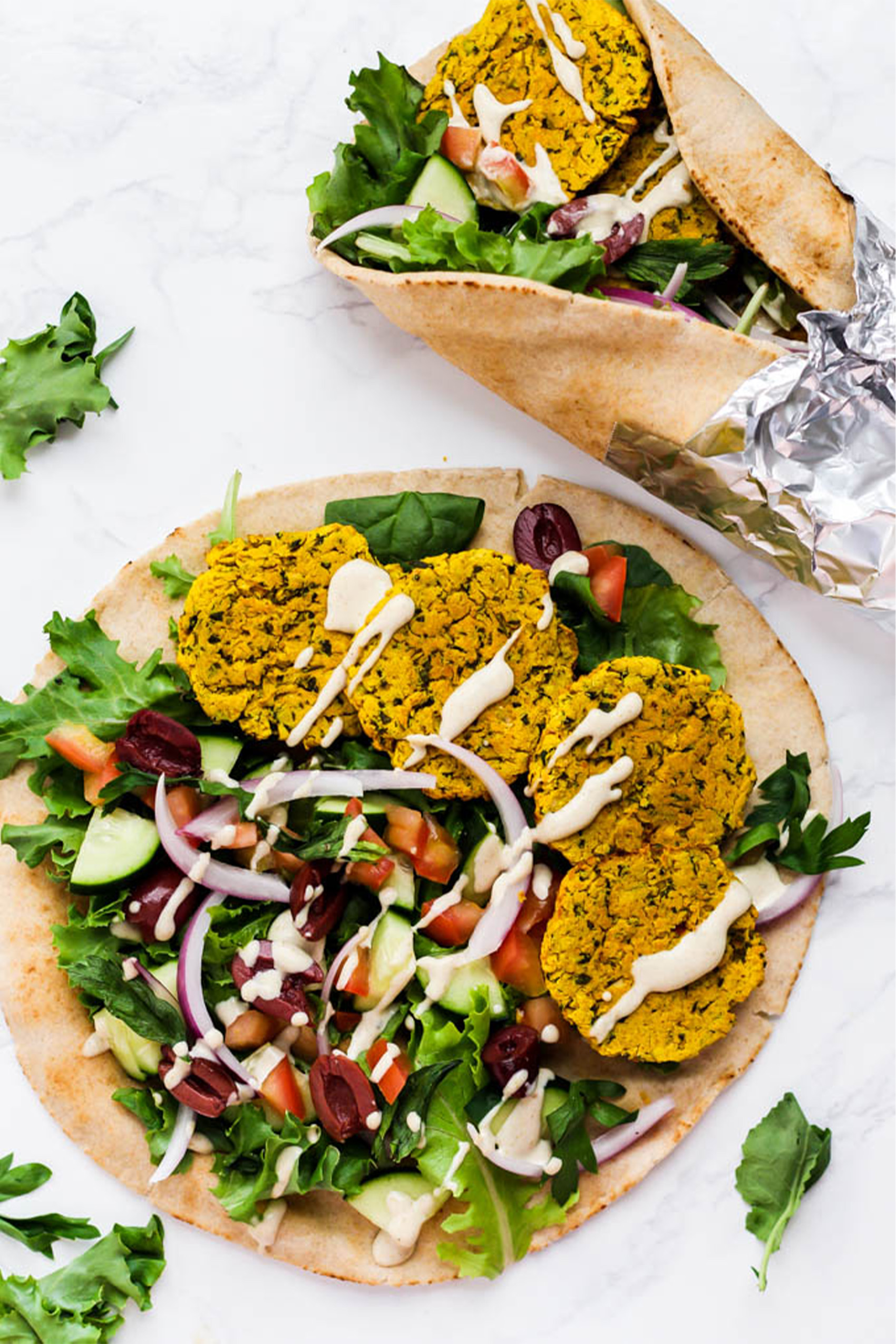 two pitas filled with greens, chopped vegetables and falafels