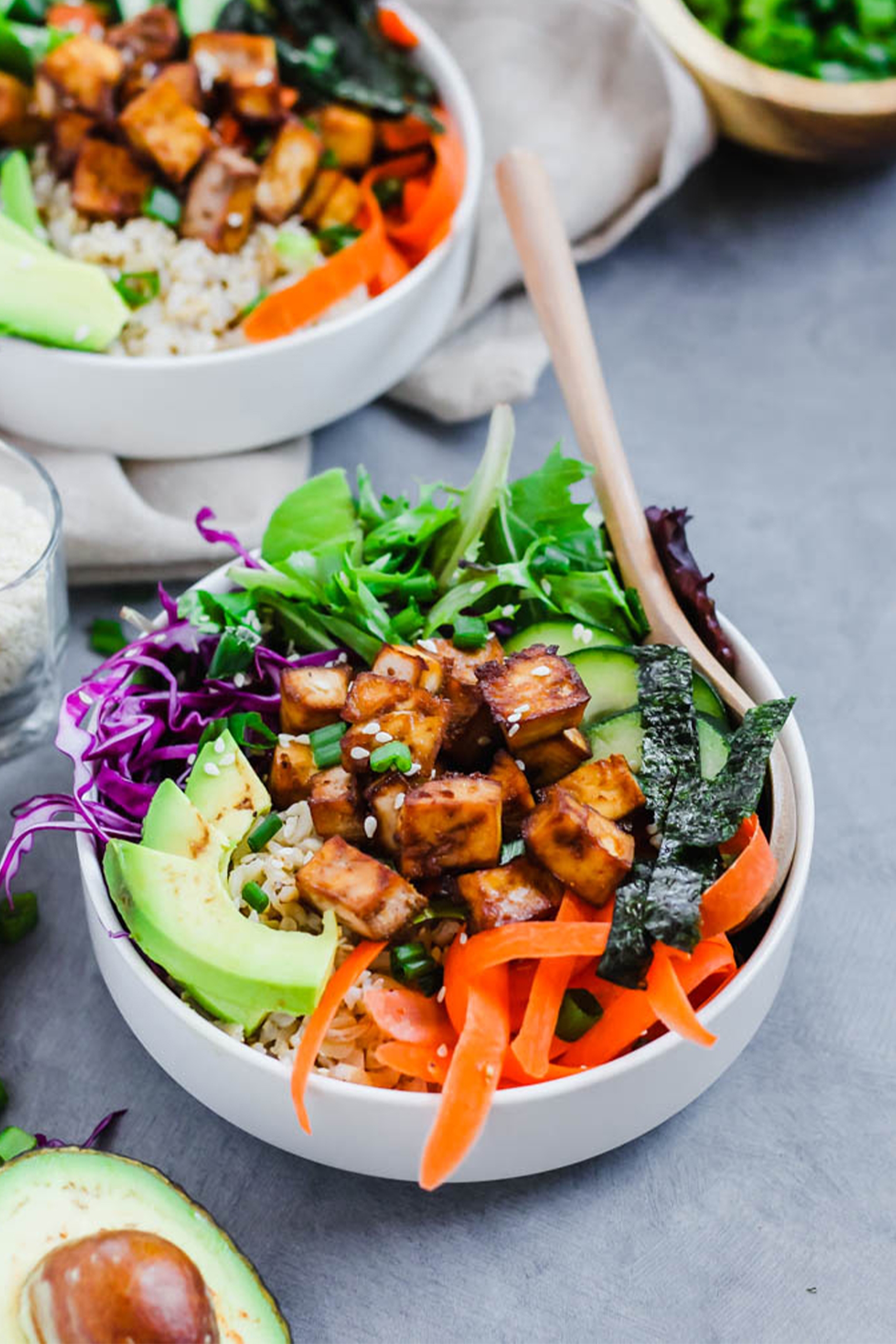 a vegan poke bowl with tofu, carrots, avocado, greens, cabbage and seaweed strips