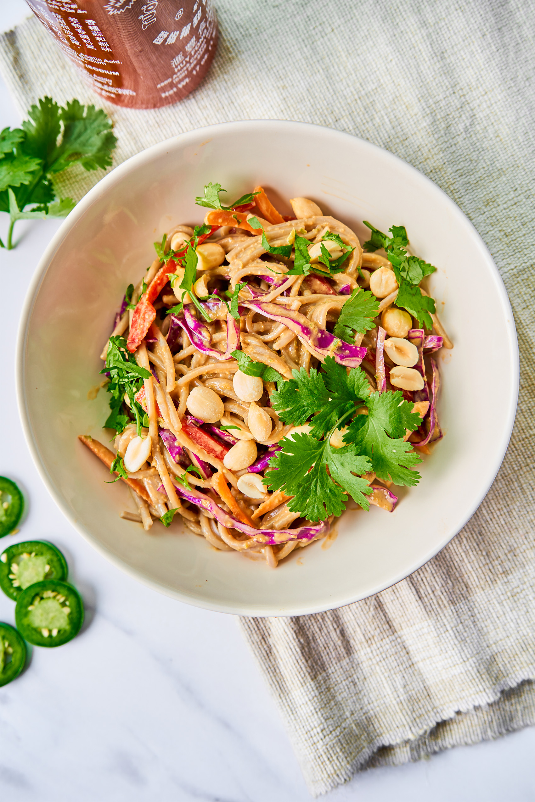 a bowl of peanut soba noodles topped with cilantro and jalapeno slices