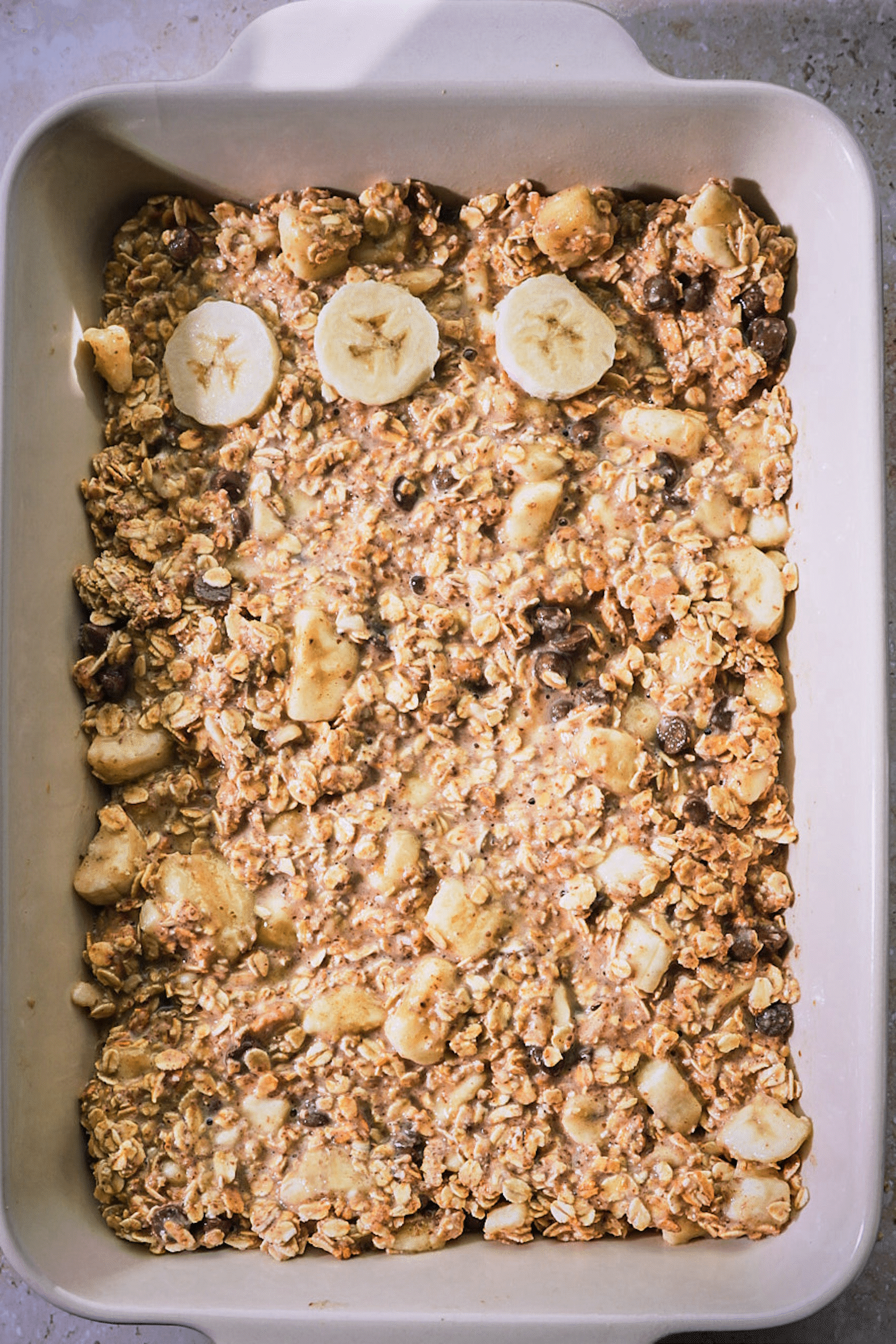 a tray of baked oatmeal being topped with sliced bananas
