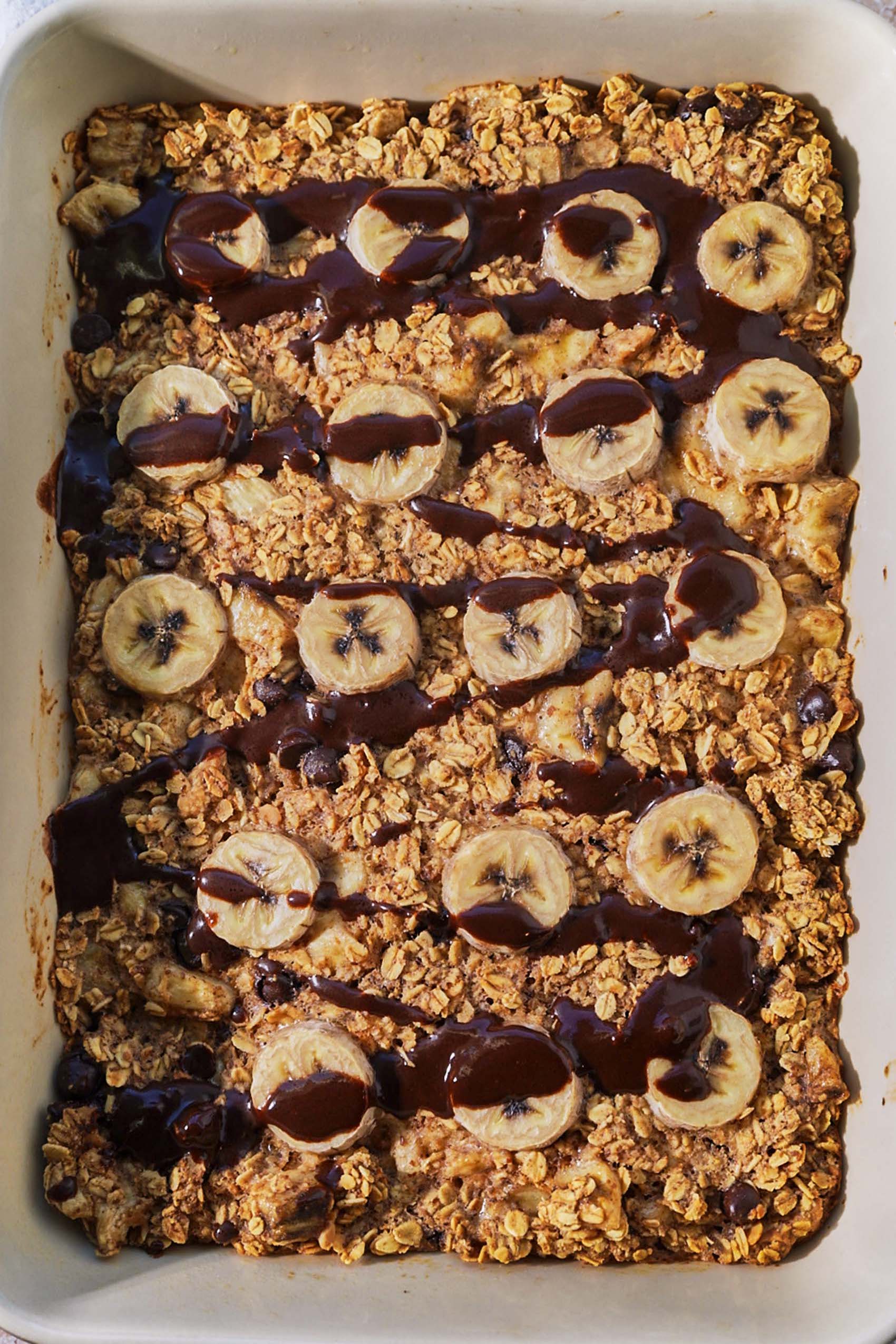 a pan of baked oatmeal topped with banana slices and chocolate sauce