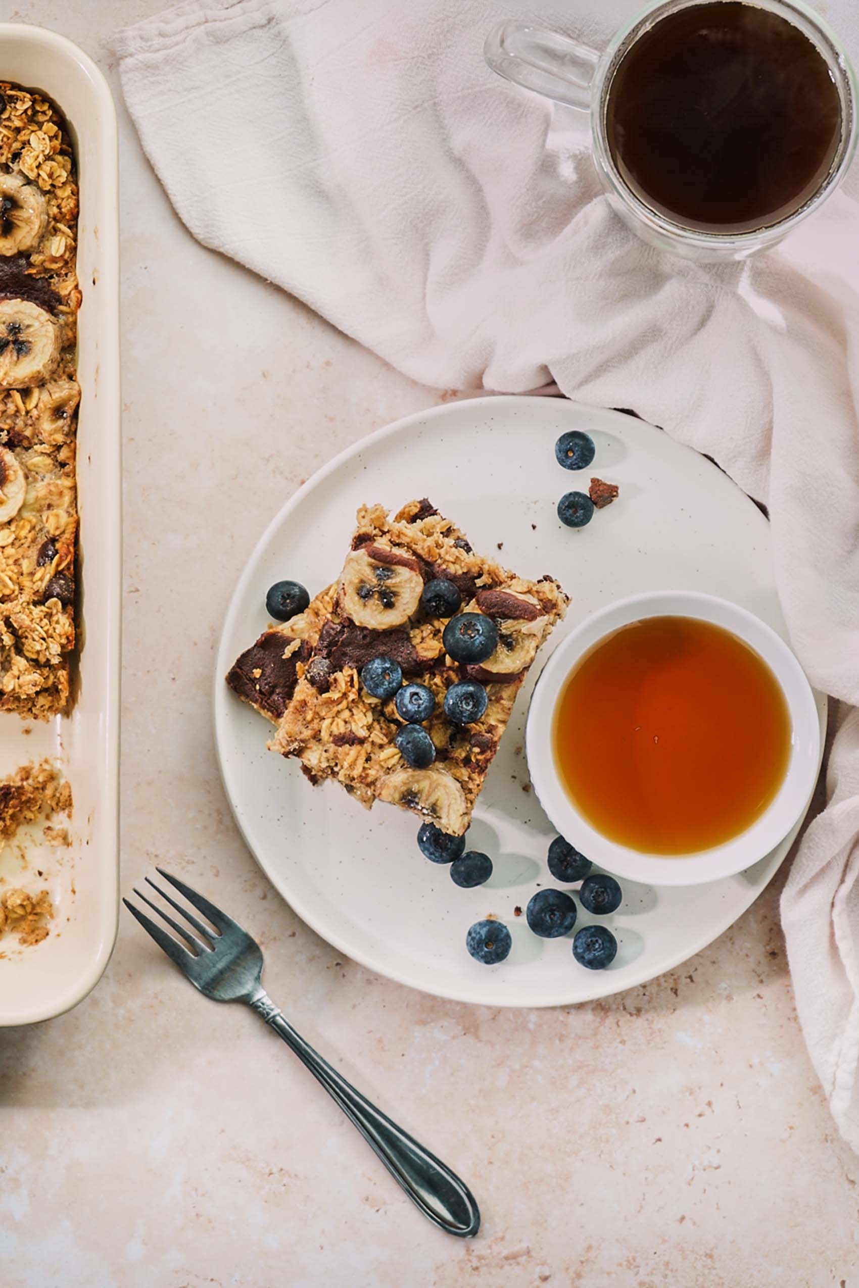 a slice of baked oatmeal with sliced bananas, blueberries and maple syrup