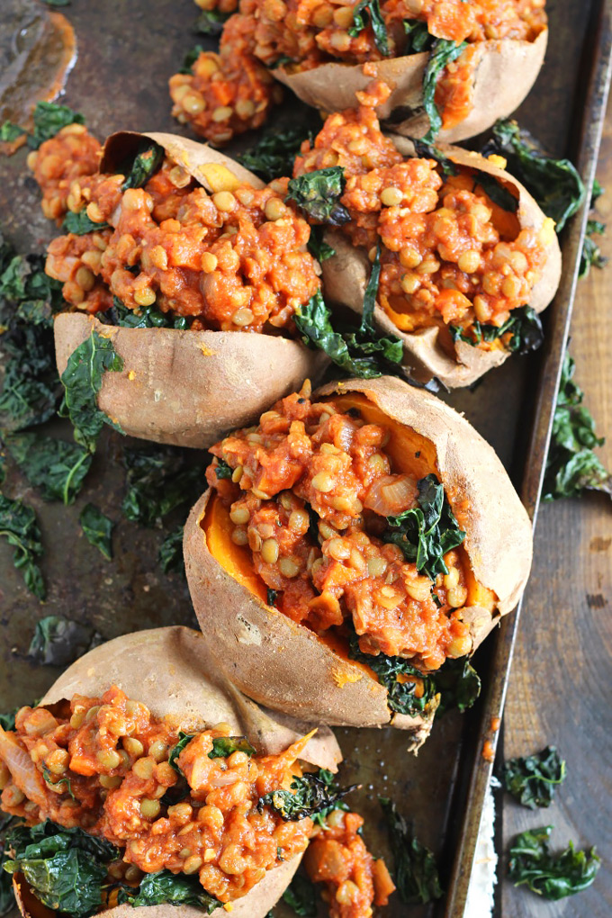 a sheet tray full of sweet potatoes, all stuffed with a bbq lentil filling and topped with kale