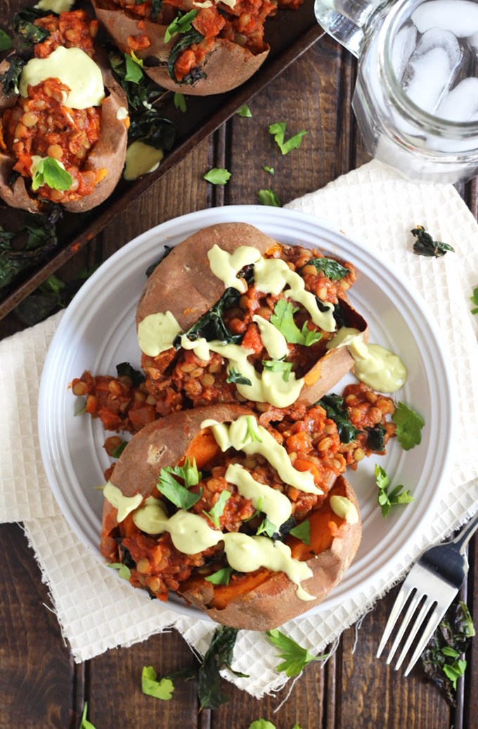 a plate of sweet potatoes filled with barbecue lentils and topped with a drizzle of avocado sauce