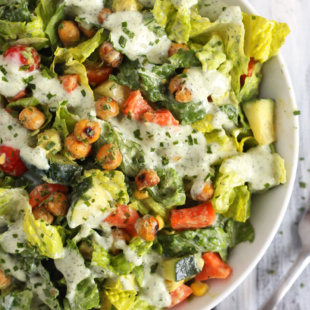 a bowl of chopped salad topped with a vegan ranch dressing and crispy chickpeas