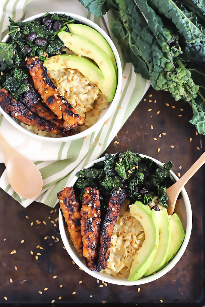 two bowls of oats topped with sauteed kale and black beans, avocado and tempeh bacon slices