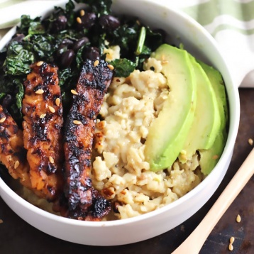 a bowl of oatmeal topped with tempeh, avocado, sauteed greens and black beans