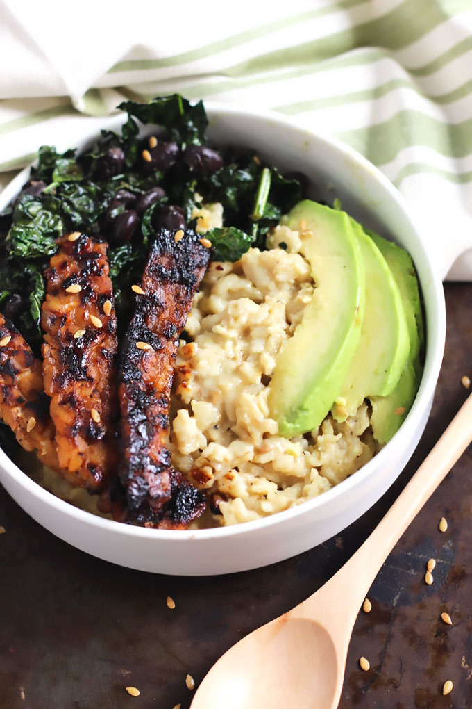 a bowl of oatmeal topped with tempeh, avocado, sauteed greens and black beans