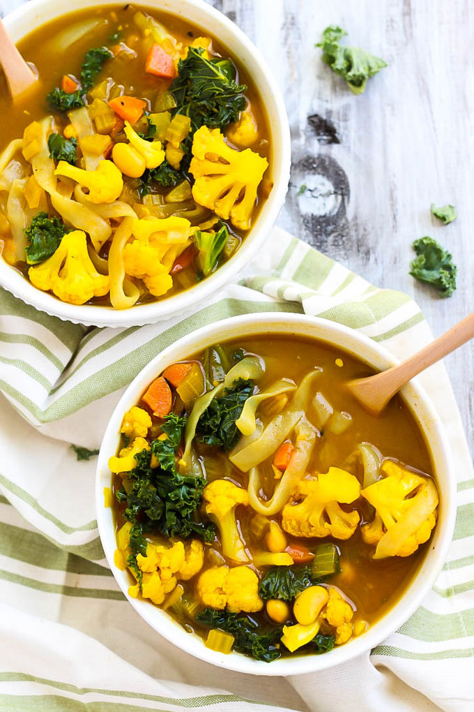 two bowls of vegetable soup with greens, cauliflower and beans