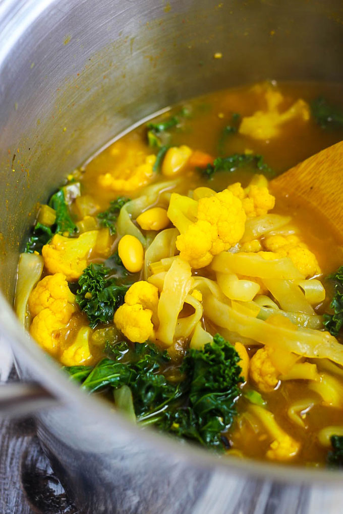 a pot of turmeric vegetable soup being stirred with a wooden spoon