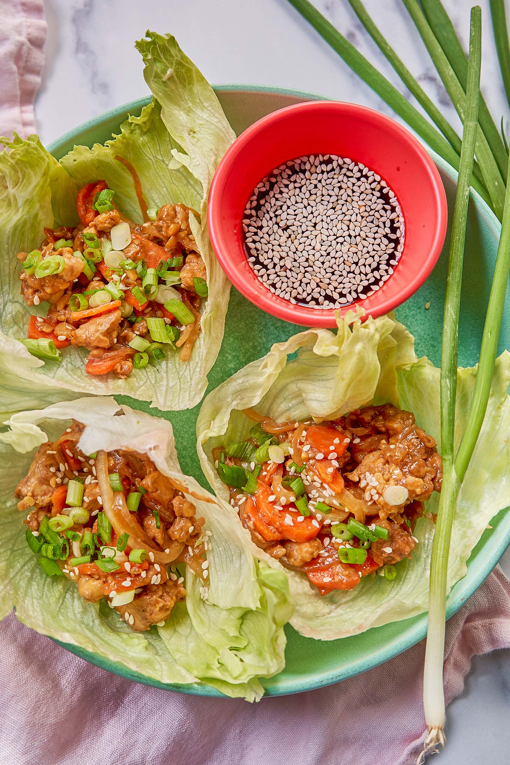 a plate of lettuce cups filled with teriyaki tempeh served with soy sauce, sesame seeds and green onion
