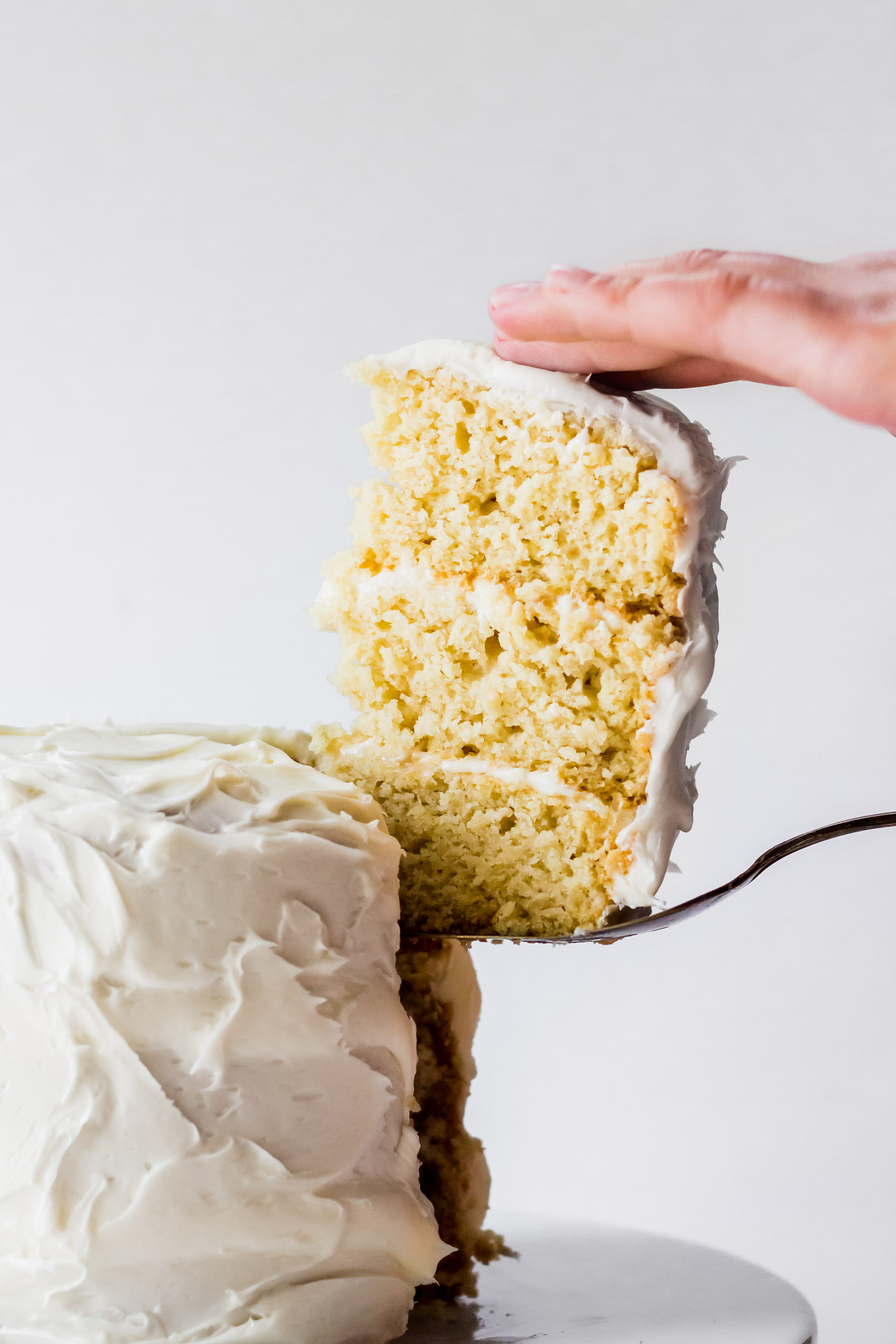 a slice of vegan vanilla cake being served from a full cake