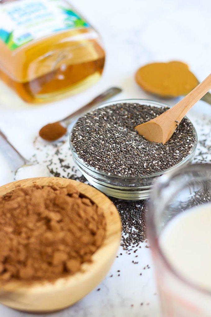 a bowl of chia seeds with a wooden spoon next to a bowl of cocoa powder