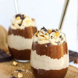 two cups of layered chocolate and peanut butter chia puddings with sliced bananas and chocolate on top
