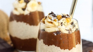 two cups of layered chocolate and peanut butter chia puddings with sliced bananas and chocolate on top