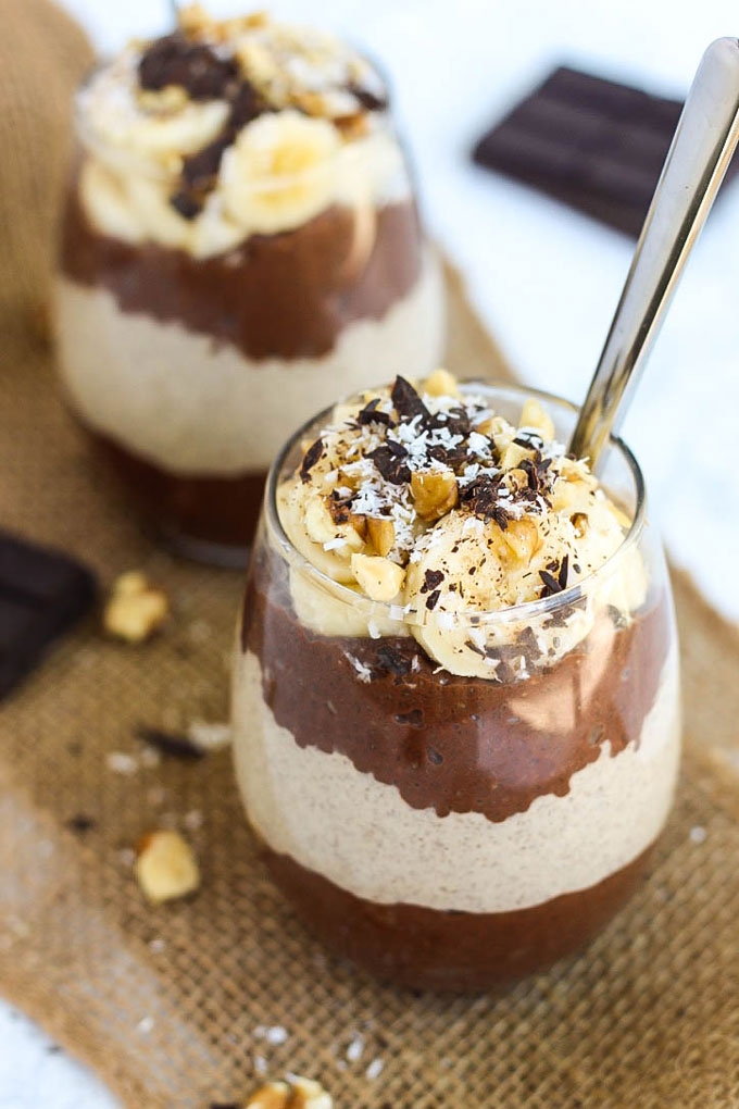 two cups filled with chocolate peanut butter chia pudding topped with peanuts, sliced banana and chocolate