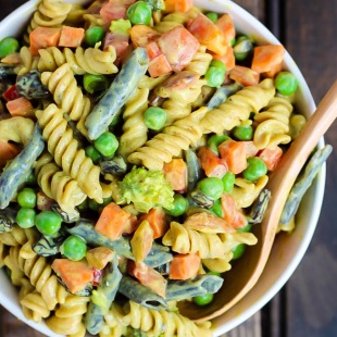 a bowl of vegan pasta salad with legume pasta, green beans, bell pepper, peas, broccoli and a silken tofu curry sauce