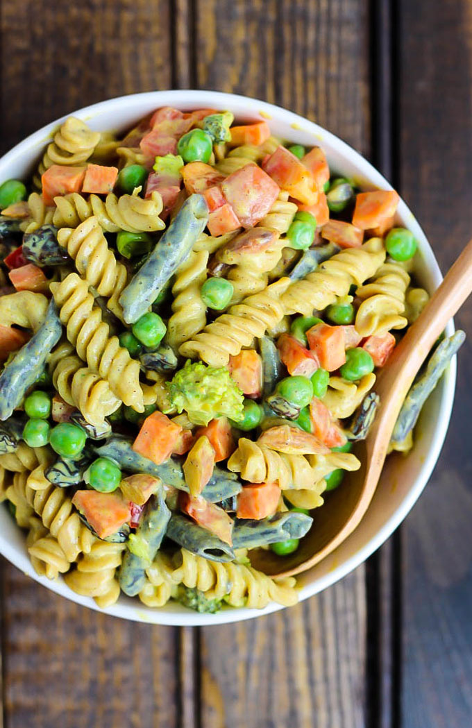 a bowl of vegan pasta salad with legume pasta, green beans, bell pepper, peas, broccoli and a silken tofu curry sauce