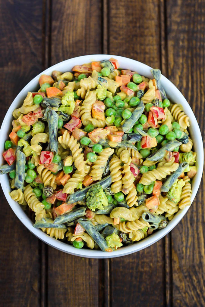 An overhead shot of a large bowl of vegan pasta salad with green beans, peppers, peas, carrots and broccoli with a curry sauce