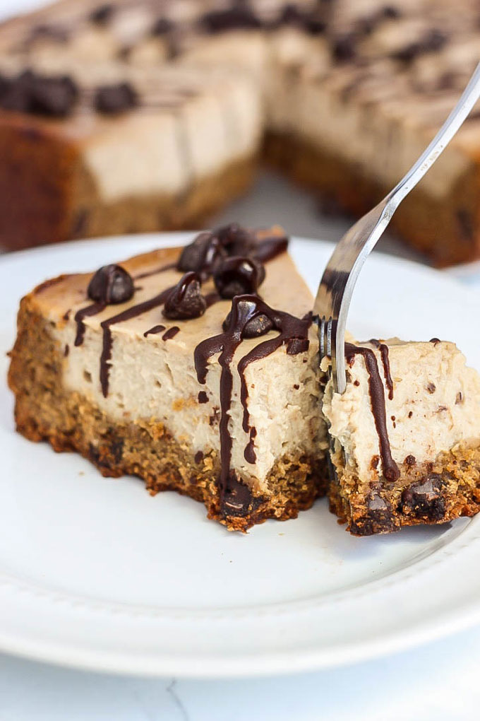 a fork cutting off a bite of vegan cheesecake that has been topped with a chocolate drizzle and chocolate chips