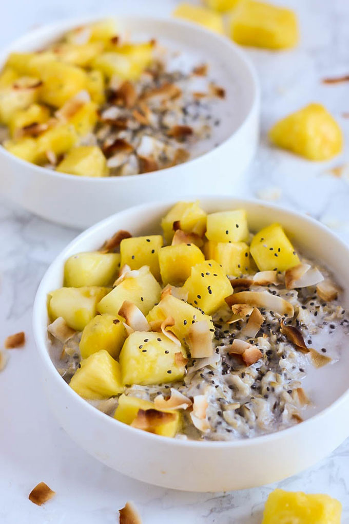 two bowls of oatmeal, each topped with chia seeds, coconut and pineapple