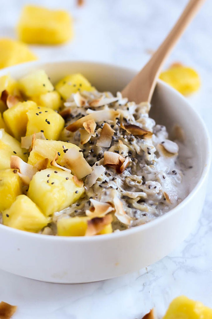 a spoon digging into a bowl of pineapple coconut oatmeal
