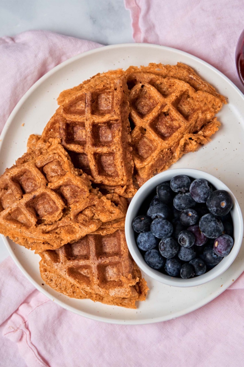 a plate of waffles served with a bowl of blueberries