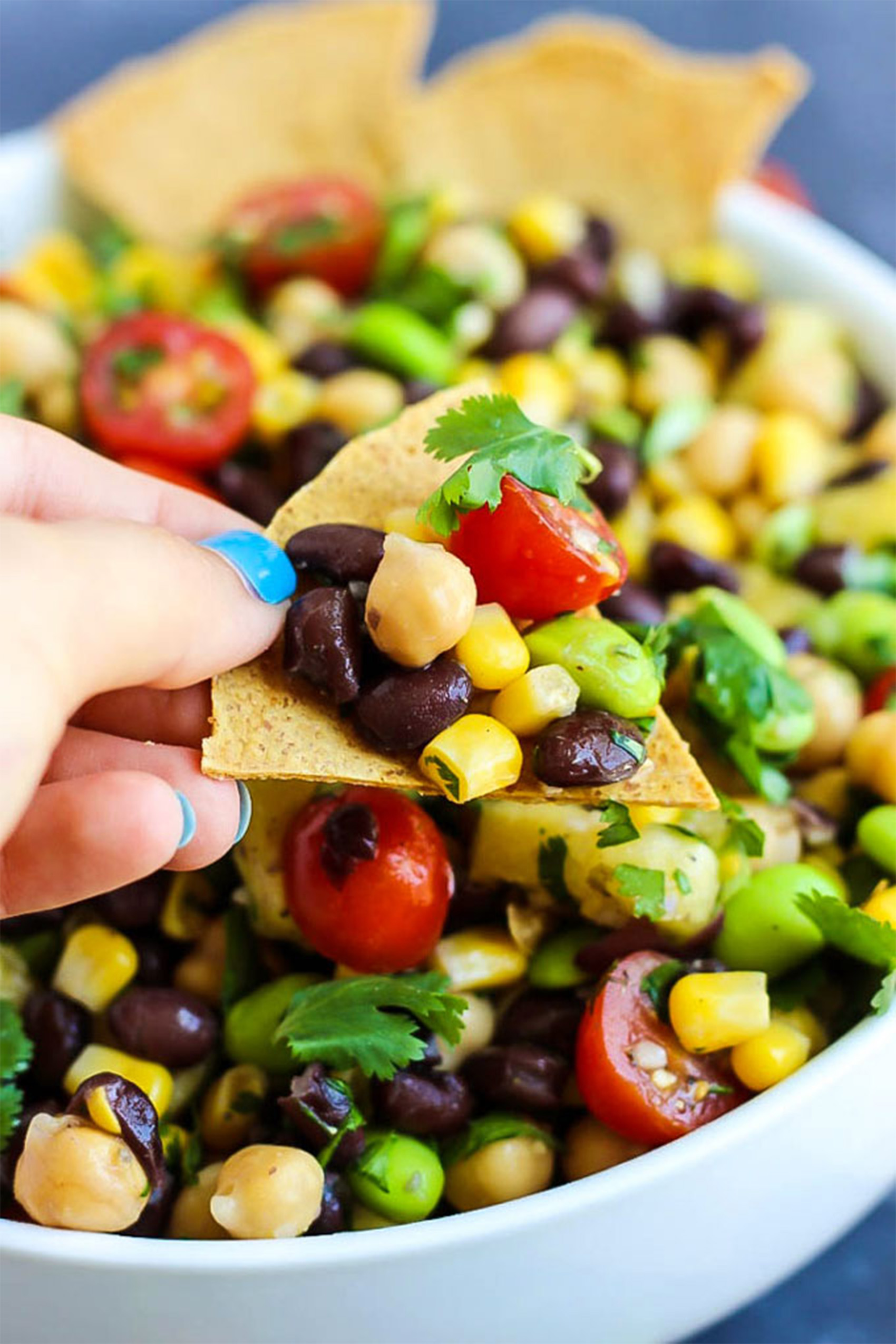 a hand holding a tortilla chip topped with three bean salad