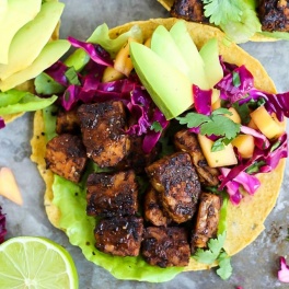 A smoky tempeh tostada topped with mango cabbage slaw and sliced avocado