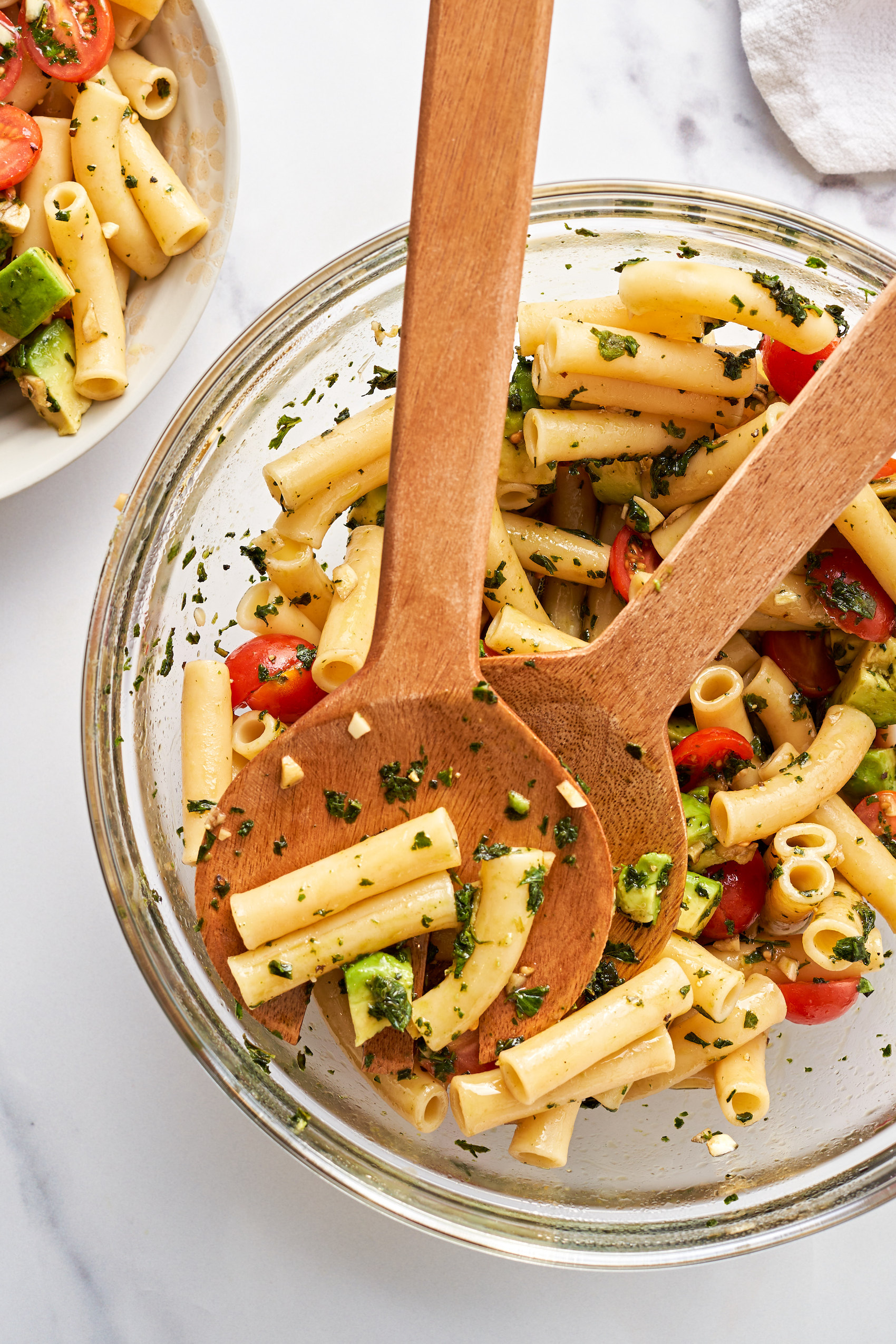 a large bowl of vegan pasta salad being tossed with wooden salad spoons