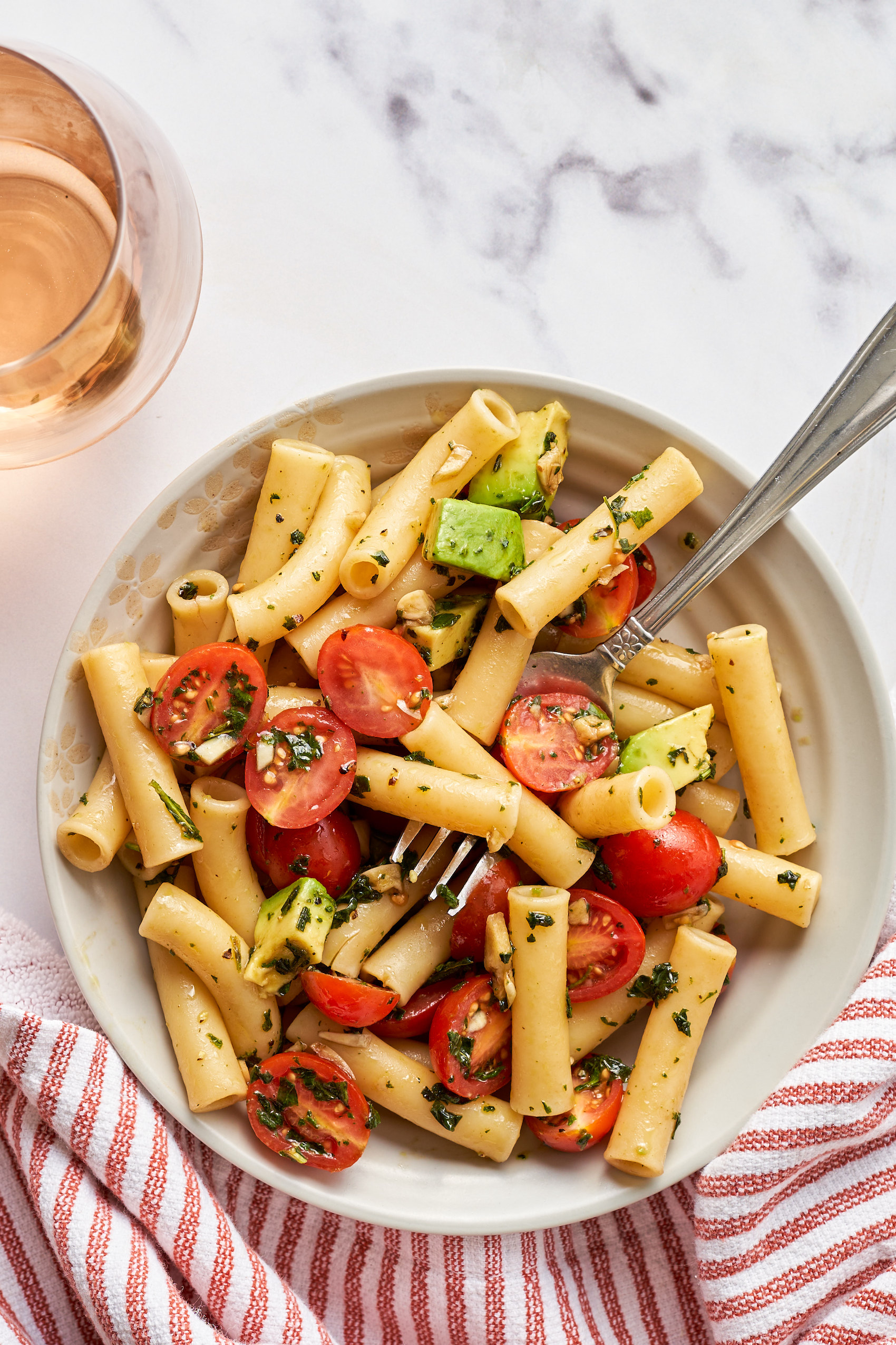 a fork digging into a bowl of vegan caprese pasta salad