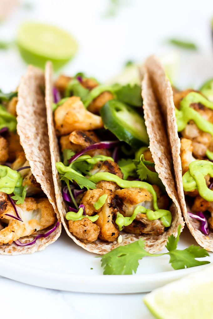 a plate of three cauliflower tacos topped with avocado cilantro sauce