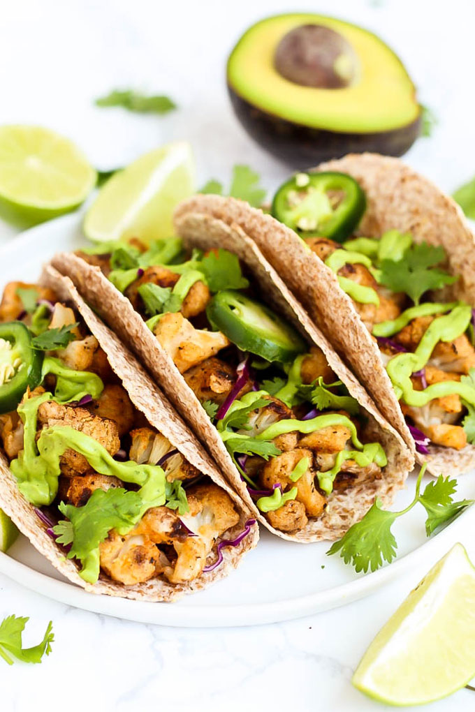 a plate of vegan tacos filled with roasted cauliflower, avocado sauce, and jalapenos