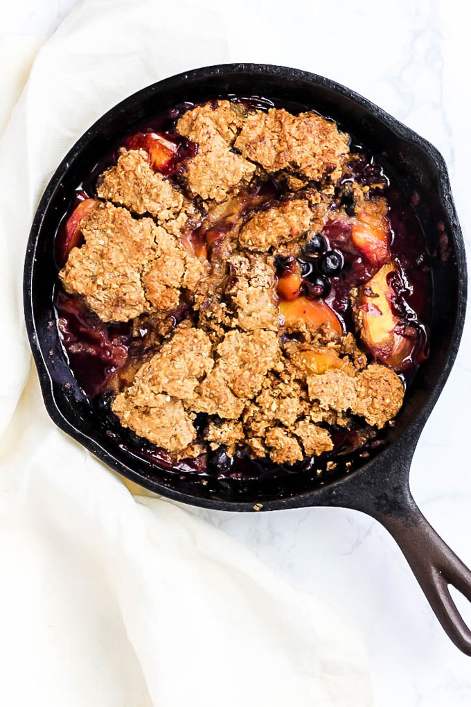 An overhead shot of a cast iron skillet of vegan and gluten-free blueberry peach cobbler