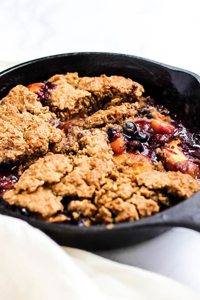 A cast iron skillet holding a blueberry peach cobbler