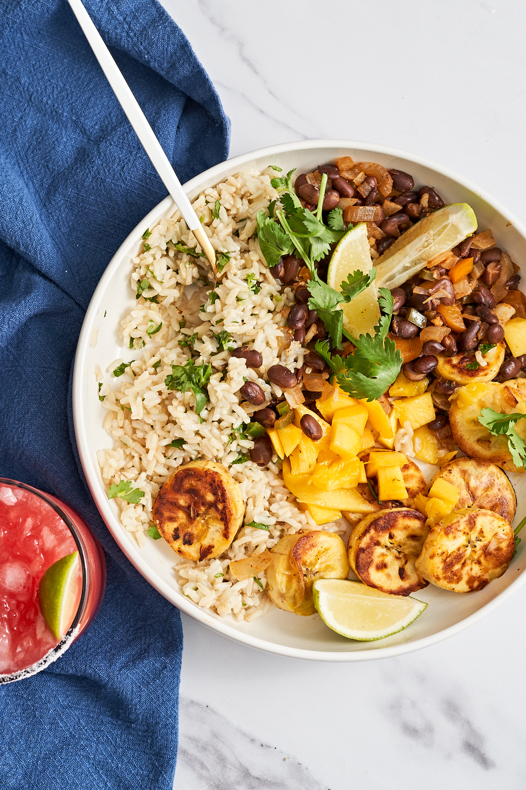 a fork digging into a bowl of black beans, rice, plantains and mango