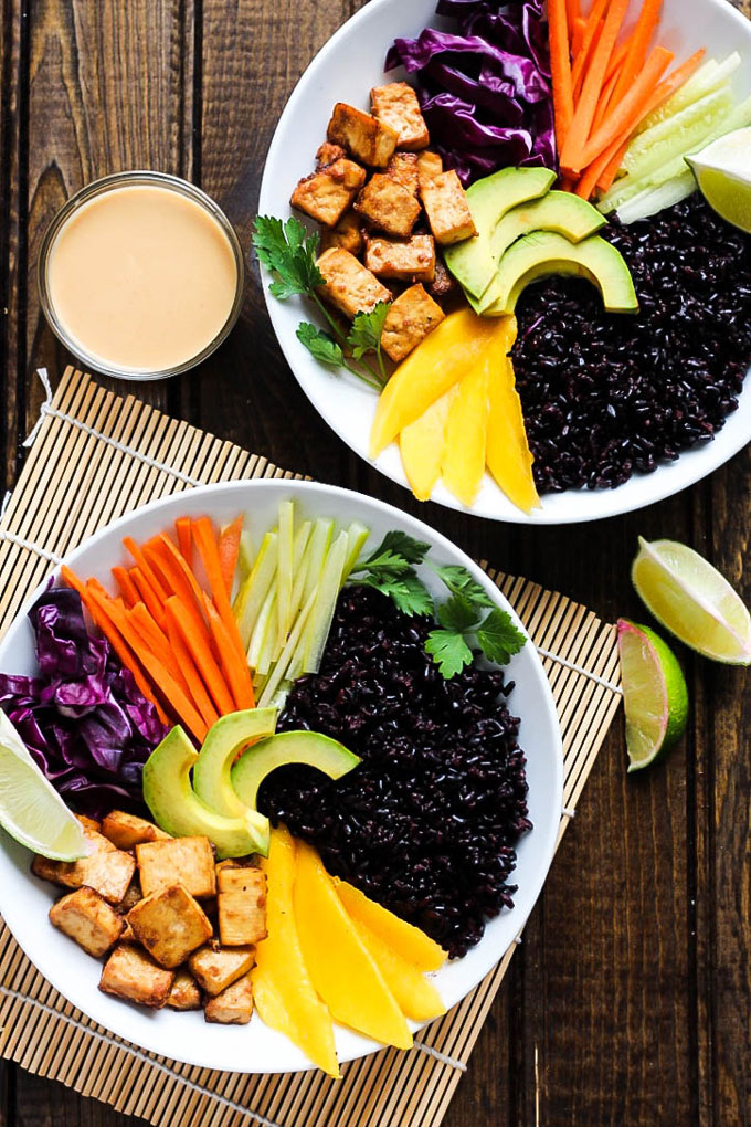 Two power bowls filled with black rice, mango, avocado, cabbage, carrots, celery, tofu and served with a tahini sriracha sauce